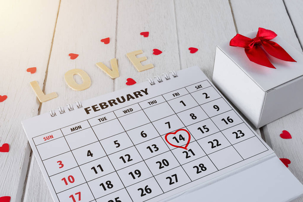 Calendar page with red hand written heart highlight on February 14 of Saint Valentines day with red Heart shape, Gift box, Wooden letters word "LOVE" on white wooden table - Foto, Imagem