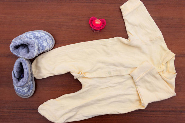Babybekleidung, Stiefeletten und Beruhigungsmittel auf Holzuntergrund. Kit für Neugeborene - Foto, Bild