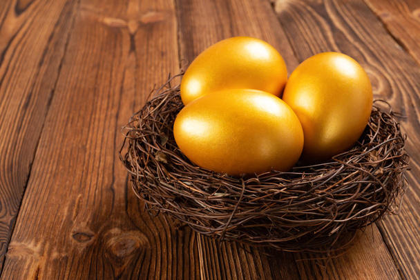 gouden eieren op een nest op houten achtergrond - Foto, afbeelding