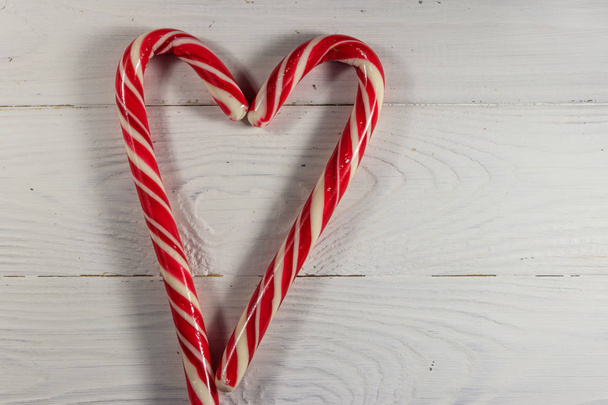 Two holiday candy canes in the shape of a heart on white wooden table. Top view - Foto, Bild