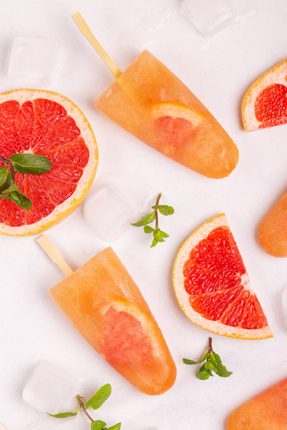 Homemade grapefruit popsicle with ripe grapefruit slices and fresh mint on light marble background. Healthy desserts. Lactose free ice cream. - Photo, Image