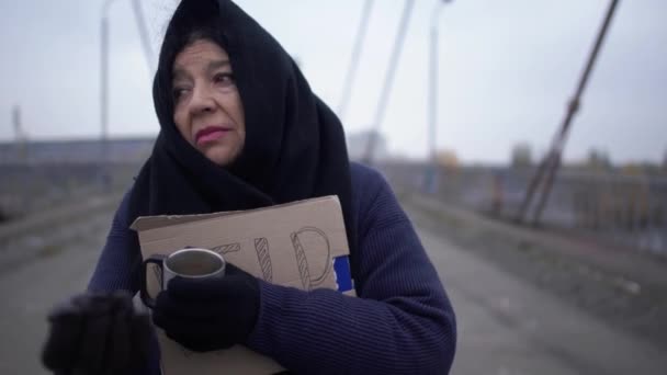 Woman gives alms to a beggar standing on the bridge in cold windy grey weather asking for alms and and charity - Filmagem, Vídeo