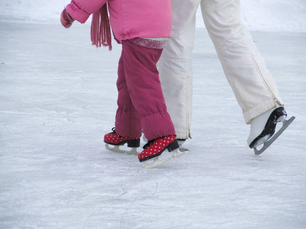 Mom teaches her little daughter to skate on the rink on a winter day - Фото, изображение