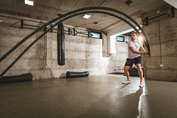 Young man doing strength training using heavy ropes at gym - Valokuva, kuva