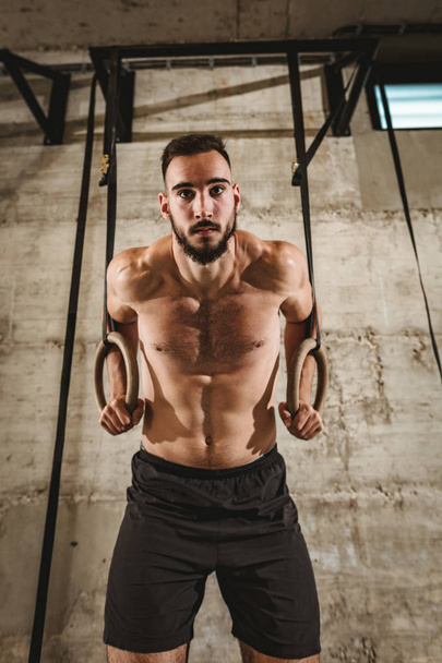 jovem muscular homem fazendo exercício no ginasta anéis no ginásio
 - Foto, Imagem