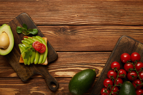 top view of toast with avocado and cherry tomatoes on wooden background - Photo, Image