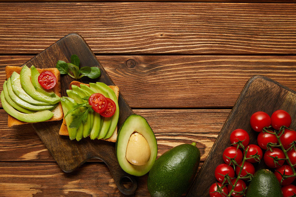 top view of toasts with avocados, cherry tomatoes on wooden background - Foto, afbeelding
