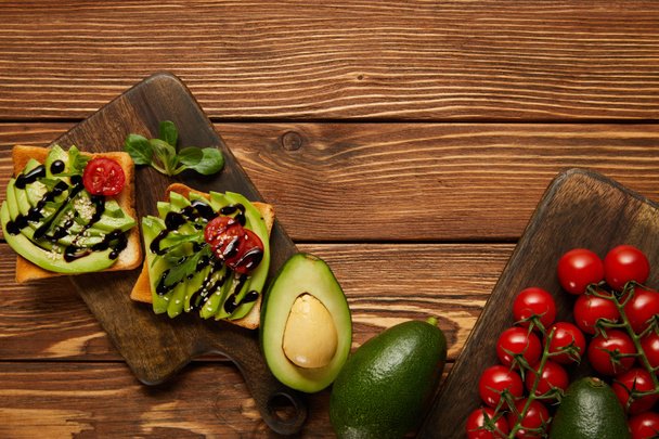top view of toasts with avocados, cherry tomatoes on wooden background - Фото, изображение