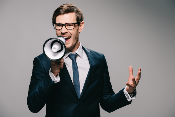 irritated businessman in suit screaming in megaphone on grey background - Photo, Image