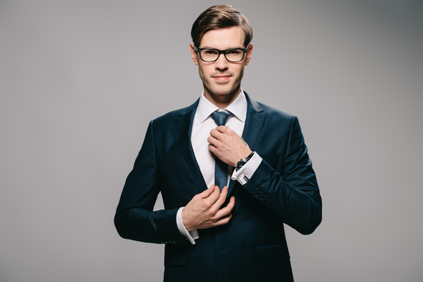 handsome businessman in suit touching tie on grey background  - Foto, Imagem
