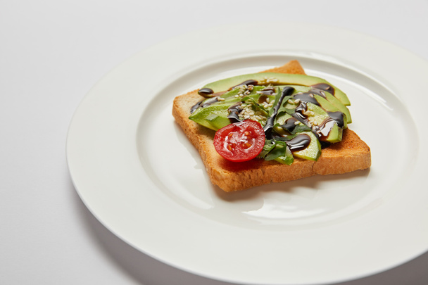 messa a fuoco selettiva di pane tostato con avocado e pomodoro ciliegia su piatto bianco e sfondo grigio
 - Foto, immagini