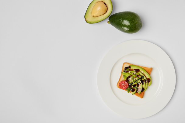top view of toast with avocados and cherry tomato on white plate on grey background - Photo, Image