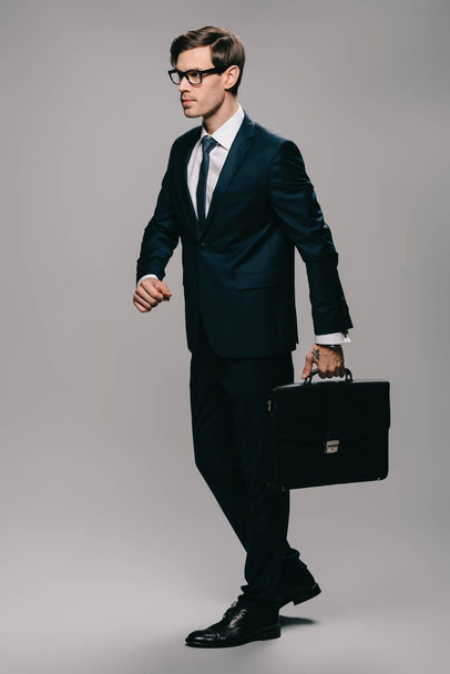 confident businessman in suit walking with briefcase on grey background  - Фото, изображение