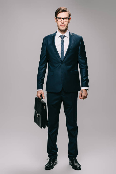 confident businessman in suit holding briefcase on grey background  - Foto, imagen