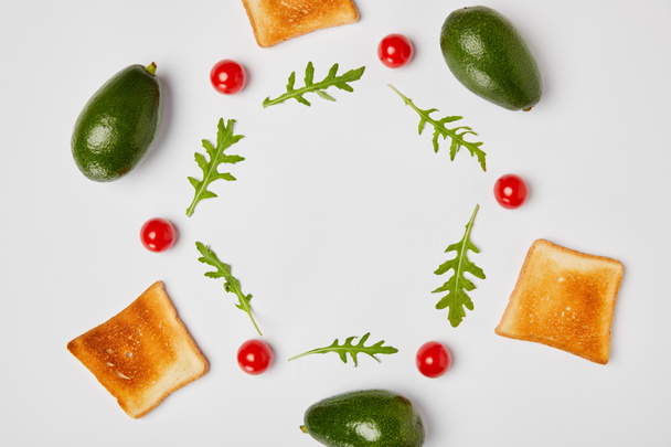 top view of avocados, arugulas leaves, toasts and cherry tomatoes on grey background - Foto, afbeelding