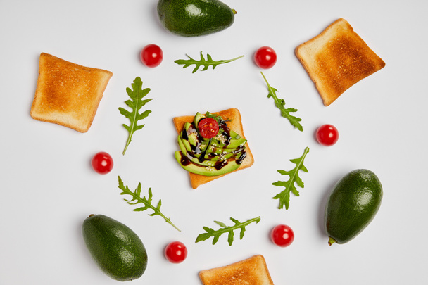 top view of toasts with avocados, cherry tomatoes and arugulas leaves on grey background - Fotografie, Obrázek