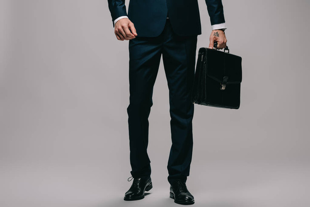 cropped view of businessman holding briefcase on grey background - Foto, imagen