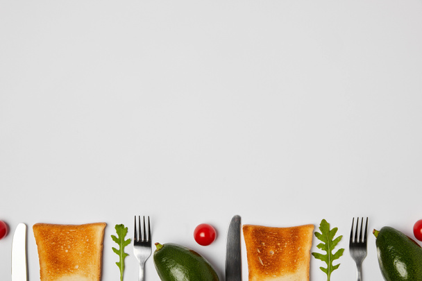 トースト、アボカド、チェリー トマトの上から見る、arugulas の葉、フォークとナイフで灰色の背景 - 写真・画像
