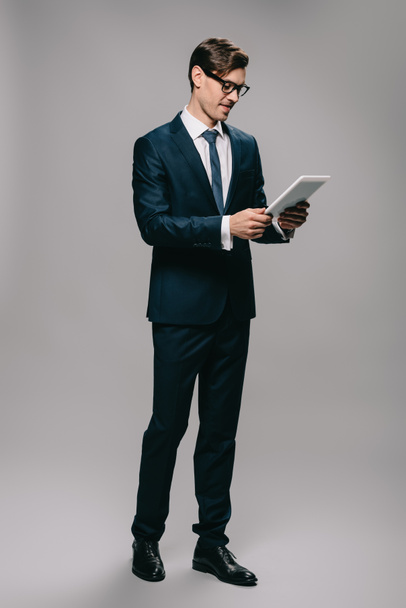 cheerful businessman in glasses holding digital tablet isolated on grey  - 写真・画像