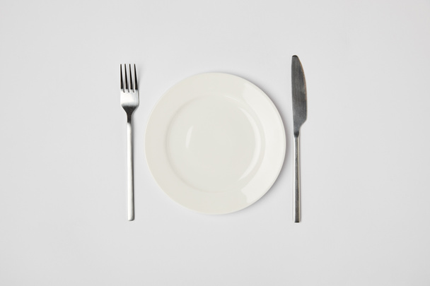top view of porcelain plate with fork and knive on grey background - Foto, immagini