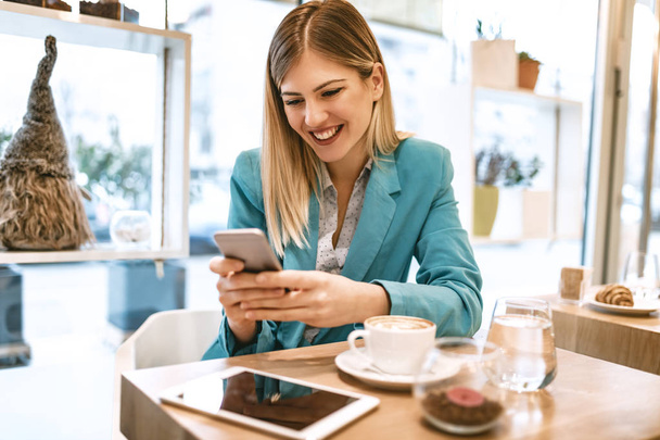 Young smiling businesswoman on coffee break in cafe using smartphone  - 写真・画像