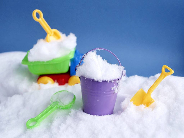 Children's toy truck with snow, toy bucket and shovel on the snow, blue background - Photo, Image