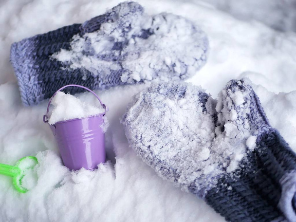 Manoplas de lana en la nieve, un cubo de juguete y una pala en la nieve, vacaciones de invierno estacionales
 - Foto, imagen