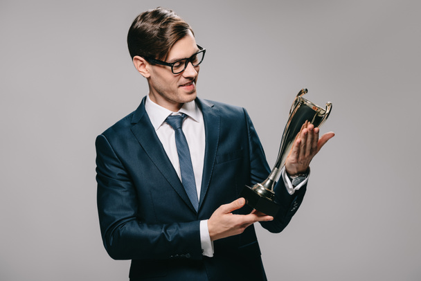 handsome businessman in glasses looking at trophy isolated on grey - Fotografie, Obrázek