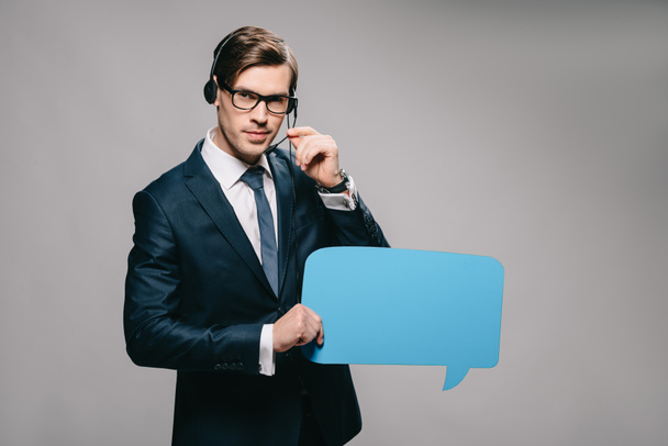 serious man in suit wearing headset and holding speech bubble on grey background  - Fotografie, Obrázek
