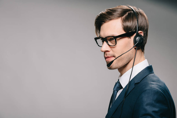 handsome man in suit and glasses wearing headset on grey background  - Valokuva, kuva
