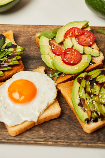 selective focus of toasts with scrambled egg, cherry tomatoes and avocado on wooden background - Foto, afbeelding