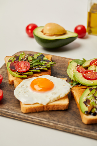 selective focus of cutting board with toasts, scrambled egg, cherry tomatoes and avocado on grey background - Foto, immagini