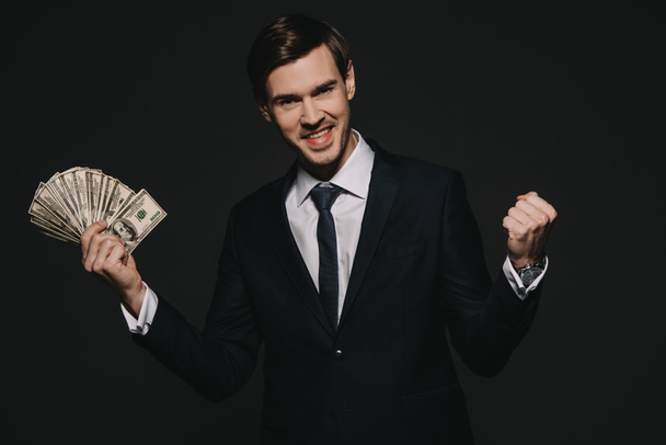 χαρούμενα επιχειρηματίας κρατώντας banknoted δολάριο στα χέρια που απομονώνονται σε μαύρο - Φωτογραφία, εικόνα