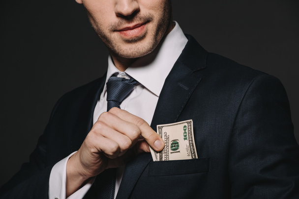 cropped view of businessman putting dollar banknote in pocket isolated on black - Foto, Imagem