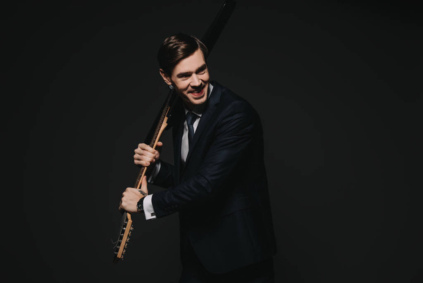 cheerful businessman holding electronic guitar in hands isolated on black - Fotografie, Obrázek