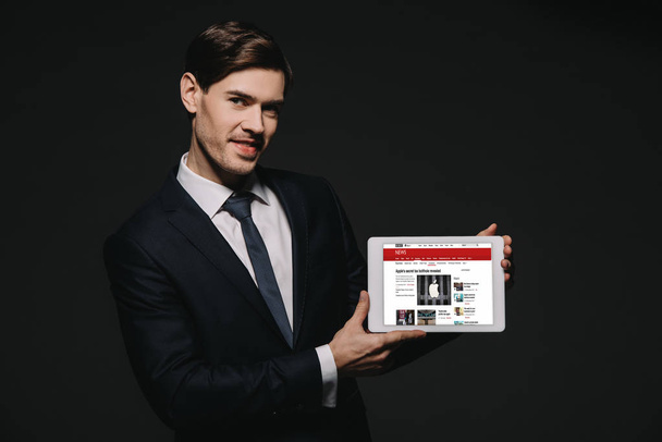 cheerful businessman holding digital tablet with bbc news app in screen isolated on black - Foto, afbeelding