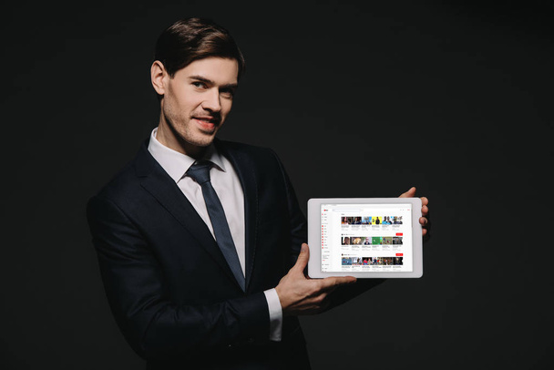 cheerful businessman holding digital tablet with youtube app in screen isolated on black - Fotografie, Obrázek