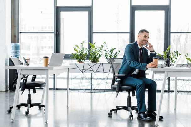 бізнесмен тримає паперовий стаканчик під час розмови на смартфоні в сучасному офісі
  - Фото, зображення