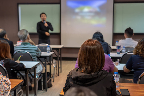 Задняя сторона аудитории слушает азиатского спикера в повседневном костюме на сцене перед залом в конференц-зале, концепции бизнеса и образования
 - Фото, изображение