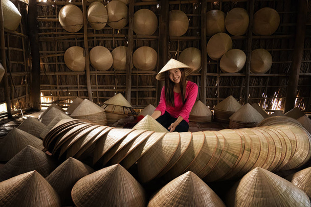 asiatische Reisende Handwerkerin, die den traditionellen vietnamesischen Hut im alten traditionellen Haus in ap thoi phuoc Dorf, hochiminh Stadt, Vietnam, traditionelles Künstler-Konzept - Foto, Bild