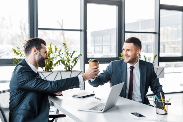 handsome businessman giving paper cup to coworker in modern office  - Foto, Bild