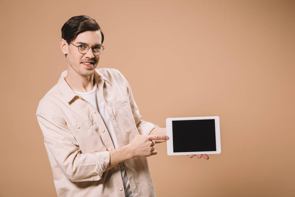 smiling man in glasses pointing with finger at digital tablet with blank screen  isolated on beige  - Foto, Imagen