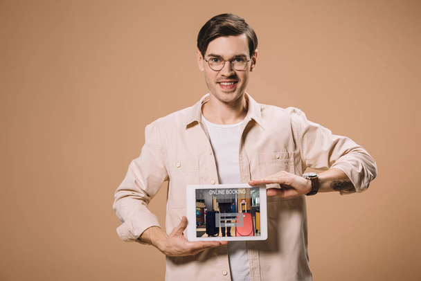 bel homme à lunettes tenant tablette numérique avec application de réservation en ligne à l'écran isolé sur beige
  - Photo, image