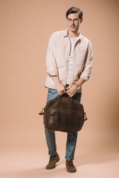 handsome man in glasses holding brown bag on beige background  - Zdjęcie, obraz