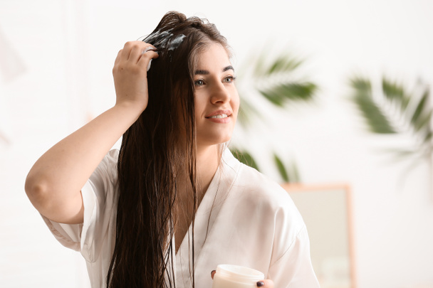 Jeune femme appliquant de la crème sur de beaux cheveux longs dans la salle de bain
 - Photo, image