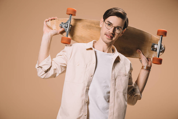 cheerful man in glasses holding skateboard while standing  isolated on beige  - Foto, Imagem