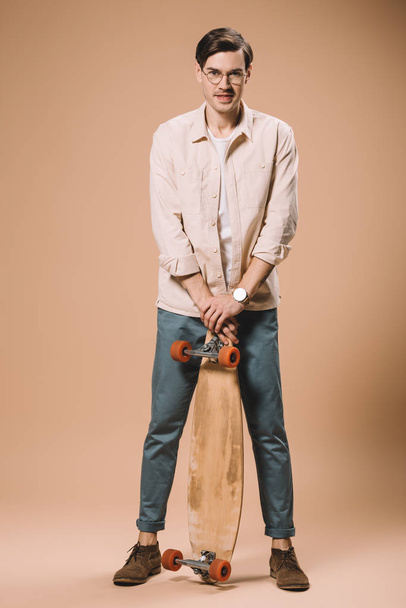 happy man in glasses holding skateboard on beige background  - Fotografie, Obrázek