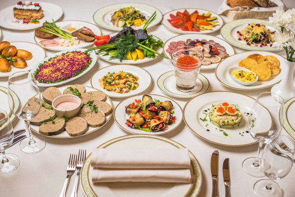 Restauranttisch mit Gourmetgerichten. Teller, Gabeln, Messer, Gläser auf einer weißen Tischdecke. Blumen in der Vase - Foto, Bild