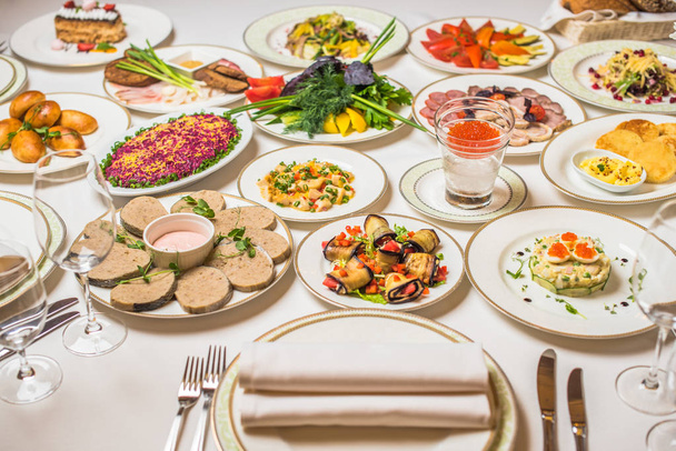 Restaurant tafel met gastronomische gerechten. Platen, vorken, messen, glazen op een wit tafellaken. Bloemen in vaas - Foto, afbeelding