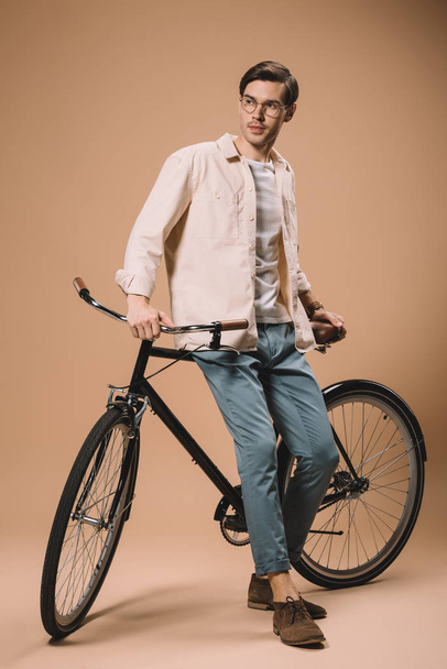 bell'uomo in occhiali in piedi vicino alla bici su sfondo beige
 - Foto, immagini